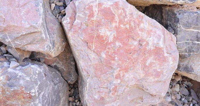 Closeup pink and gray color rough surface worn rock with white mineral streaks and areas in dry stack rock wall 4k
