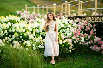 Beautiful young woman in vintage elegant dress posing among hydrangeas in a park