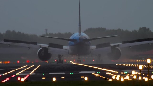 Passenger jet decelerating after touchdown, viewed from behind. Spoilers deployed, braking in progress, with runway lights glowing.