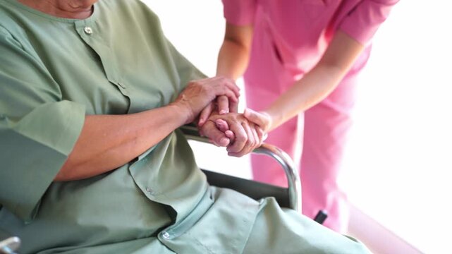 Caring Touch: A caregiver gently holds the hand of an elderly patient seated in a wheelchair, conveying empathy and compassionate support in a moment of quiet care.