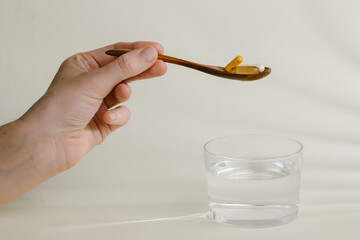 Hand holding wooden spoon with pills over glass of water