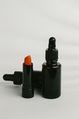 Orange lipstick and dropper bottles creating modern beauty products scene