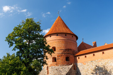 Medieval brick castle tower with red tiled roof and stone wall under blue sky, historical architecture