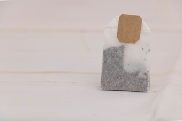 Single tea bag with paper label on light background, herbal drink ingredient for hot beverage, health and relaxation concept