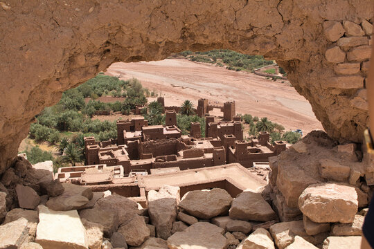 Climb to a Moroccan hilltop town - A stunning view of a traditional Moroccan fortified village and a dry riverbed from a high vantage point framed by a rocky opening.