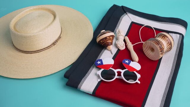 Traditional chilean huaso hat, spinning top, emboque, chilean flag sunglasses, and poncho displayed on a vibrant turquoise background