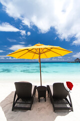 Santa Claus hat on sunbed on tropical beach with sun umbrellas and chaise longues. Christmas and New Year celebration