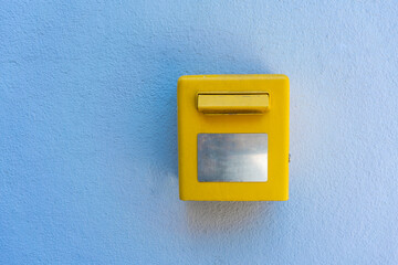 Yellow metal mailbox on a blue stone wall. Empty copy space.