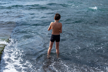 Teen boy playing in ocean waves on black volcanic sand beach, joyful summer moment, natural fun, healthy childhood, barefoot freedom