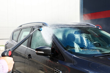 Obraz premium Car washed with a high-pressure jet under bright sunlight, emphasizing sparkling cleanliness, professional maintenance, and contemporary vehicle care (part of the “at the car wash” series).