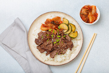 Beef bulgogi bowl dish with rice, roasted meat slices, kimchi and marinated cucumber on white background, traditional dish of Korea