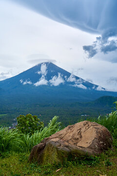 A viewpoint with a large stone and a view of the sacred volcano Agung covered with clouds on a rainy day on the island of Bali. View of the mountain.