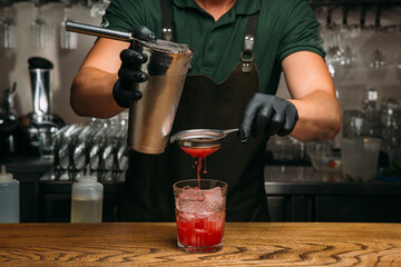 Bartender pouring cocktail into glass with ice and strainer