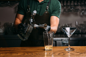Bartender pouring alcoholic drink into glass using jigger and metal pour spout