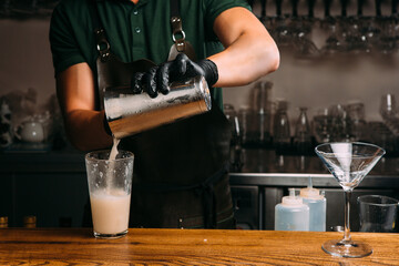 Bartender pouring cocktail into glass at bar counter