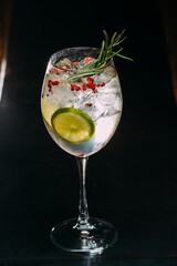 Gin and tonic cocktail decorated with lime, rosemary and red peppercorns