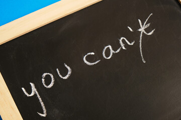 chalk inscription on daughter "you can" with crossed out letter n, chalk board on blue background
