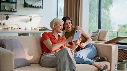 Relaxed sisters looking smartphones in house. Laughing girls using mobile phones