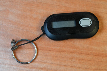 A black security token dongle rests on a wood surface with a metal keyring attached, used for multi-factor authentication and device security.
