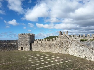 Interior courtyard of Montemor-o-Velho Castle with medieval stone walls, defensive towers, and battlements under a dramatic blue sky with clouds