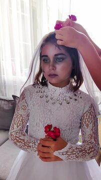 A girl in a white dress, the image of a scary bride, gets zombie makeup for Halloween