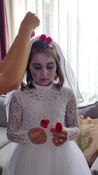 A girl in a white dress, the image of a scary bride, gets zombie makeup for Halloween