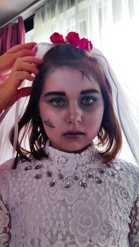 A girl in a white dress, the image of a scary bride, gets zombie makeup for Halloween