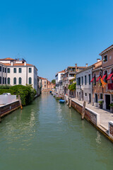 Obraz premium Peaceful Venice canal with boats and historic houses. Tranquil scene of a narrow Venice canal lined with colorful buildings, small boats, and clear blue sky on a sunny day.