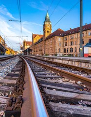 Fototapeta premium Low-angle view of train tracks leading to a historic European station, with old buildings and a clear sky