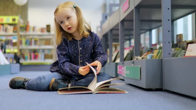 4 year old girl sitting on the floor in municipal library and reading a book
