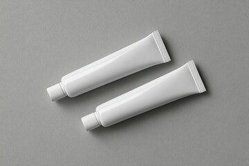 Two blank, white tubes of cosmetic or skincare product, positioned horizontally on a gray surface
