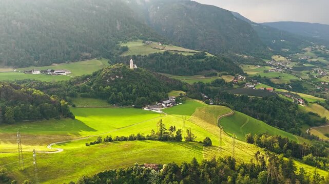 Wide meadows and grazing parcels around Chiesa di Santa Verena with a farm yard in Dolomites, South Tyrol, aerial view. Evening light across alpine countryside