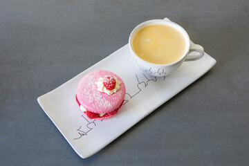 Elegant pink raspberry macaron with cream filling and fresh berries served alongside coffee on white porcelain plate. Perfect French pastry dessert presentation.