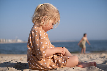 blonde girl sitting on the beach and playing alone