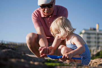 girl playing with grandfather in sand on the beach during summer holidays