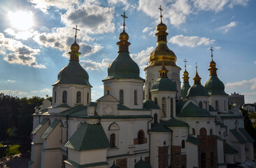 Golden and green onion domes of a historic Orthodox cathedral Saint Sophia's in Kyiv, rise against a partly cloudy blue sky