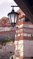 Black lantern hangs from a stone building, shaded by a dark roof overhang