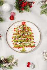 Edible Christmas tree made of kiwi and pomegranate for a festive table, an idea for decorating food and decorating dishes for children. Christmas and New Year's dishes. Banner for creativity,