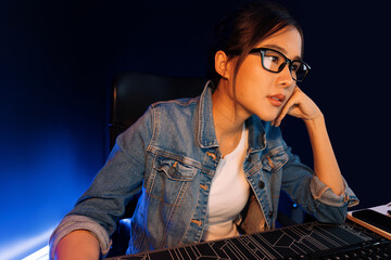 Stressful young beautiful asian creative with glasses looking on pc to search project creator social media online, planning strategy reach more viewer home at neon modern office at night. Stratagem.