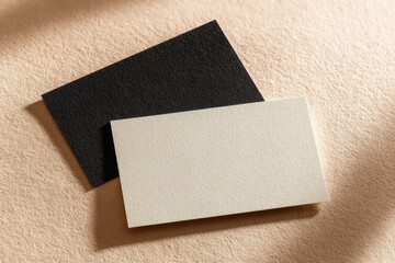 Two blank business cards, black and cream, laid on a beige surface, with subtle shadows