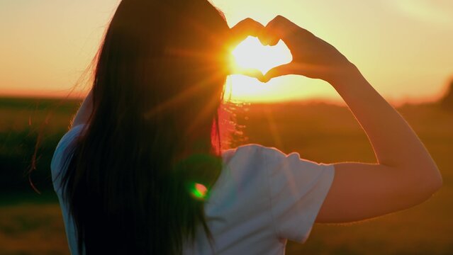 Healthy heart. Happy girl makes a heart with her fingers nature. Young woman loves travel. Girl made heart from her palms. Symbol of love in hands of teenager girls sun light. Travel, relax in nature