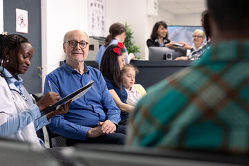 Smiling elderly man receives medical consultation in clinic waiting room. African american doctor...