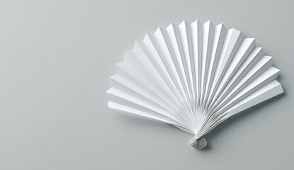 A pristine white paper fan, sharply folded, rests on a light gray surface