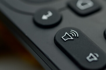 close-up of a matte black remote control, highlighting the crisp white speaker icon on the elongated volume-up button.