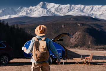 Adventurous young male enjoying mountain view with blue trailer camper