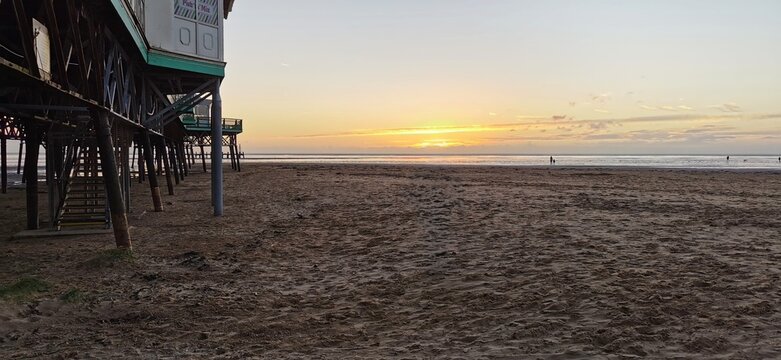 Golden tranquil sunset over Lytham St Annes sandy deserted beach. Sand, sea, sun setting. Seaside holiday pier view, stilt structure, empty coastal shoreline no people. Breathtaking dusk ocean horizon