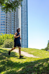 Athletic young man tackling ups and downs while jogging in an urban park with contemporary buildings