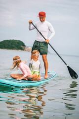 Playful summer day at beach. Dad and kids enjoying paddleboarding under sun, surrounded by tropical beauty. Freedom, smiles, and water fun.
