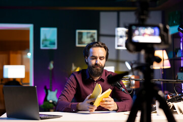 Content creator in studio reviewing newly released hardcover book from publisher, unhappy with story. Reading hobbyist filming literature video essay for new novel, not impressed with characters