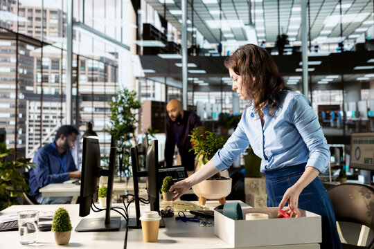New hire starting her first day at the business corporation and unpacking her belongings, placing and arranging office supplies. Hopeful enthusiastic woman newcomer joining the team.